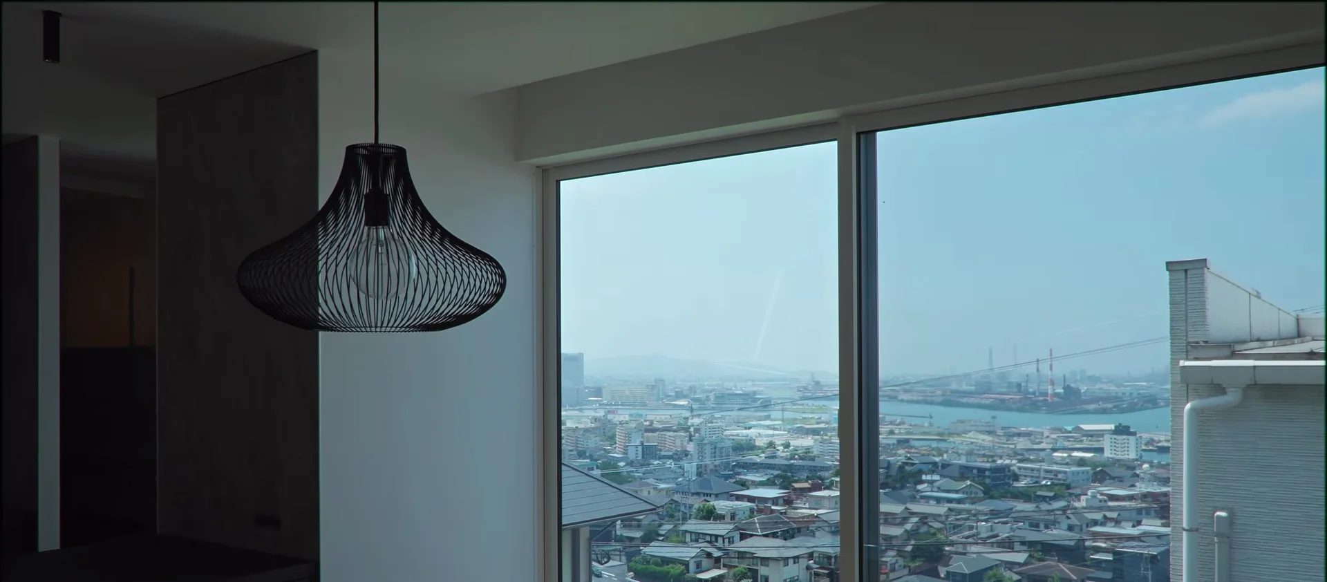 黒いワイヤーのペンダント越しに、LDK の窓の外に広がる街並みと海