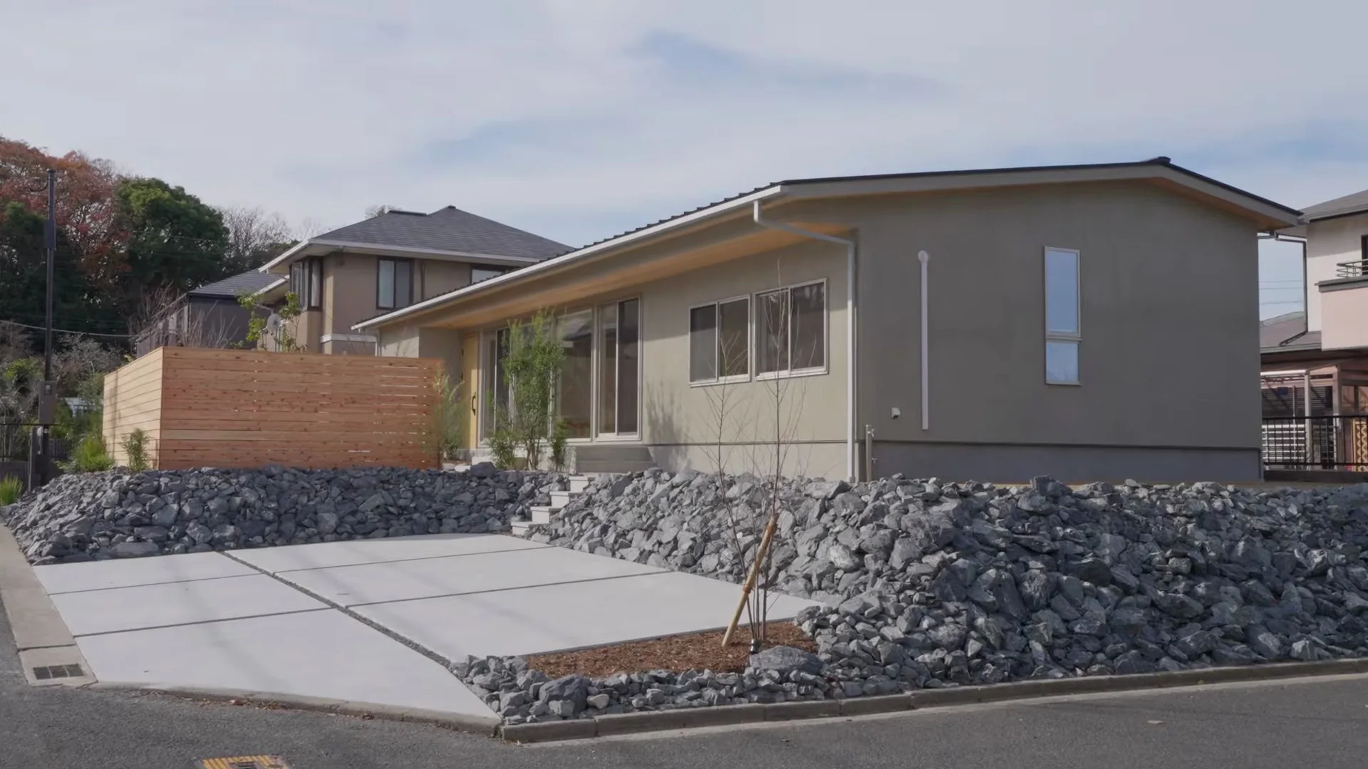 石積みの上に建つ、塗り壁と板塀の平屋の外観。手前に広い駐車場